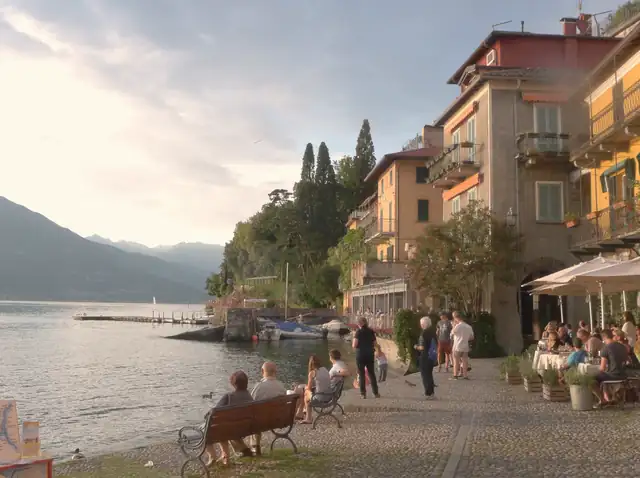 The waterfront of Varenna on Lake Como at sunset, with pastel houses and café tables